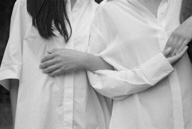 Two women in white shirts stand next to each other, arms linked, symbolizing dependent personality disorder.